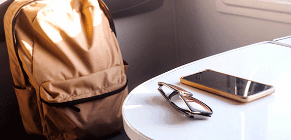 Liegengeblassener Rucksack, Sonnenbrille und Smartphone auf einem Tisch im Zug